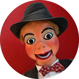 Dusty Backlog, a Mack ventriloquial figure in a gray fedora and red bow tie