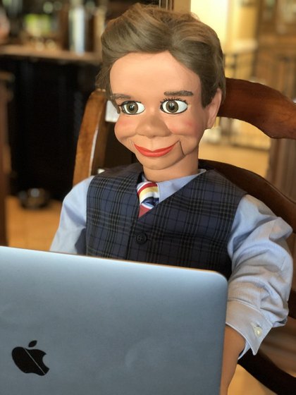 Freddy Fiddlesticks, a ventriloquial figure in a waistcoat and tie, seated at a laptop