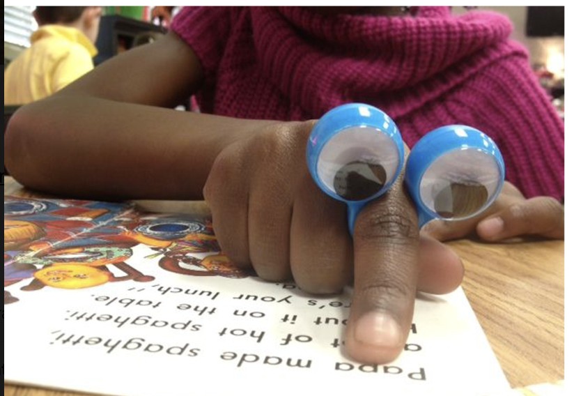 Child using a blue peeper puppet over one finger while reading a book